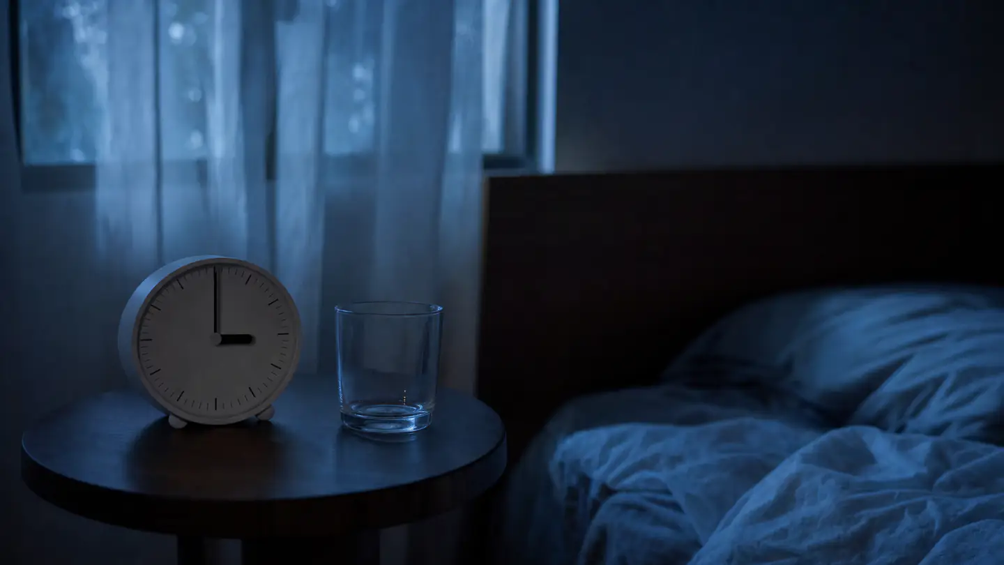 Reloj despertador marcando las 3 de la madrugada en el buró de una recámara en penumbra